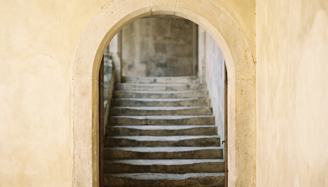 An old stone archway opening onto a worn stone stair, the steps deeply hollowed by centuries of feet